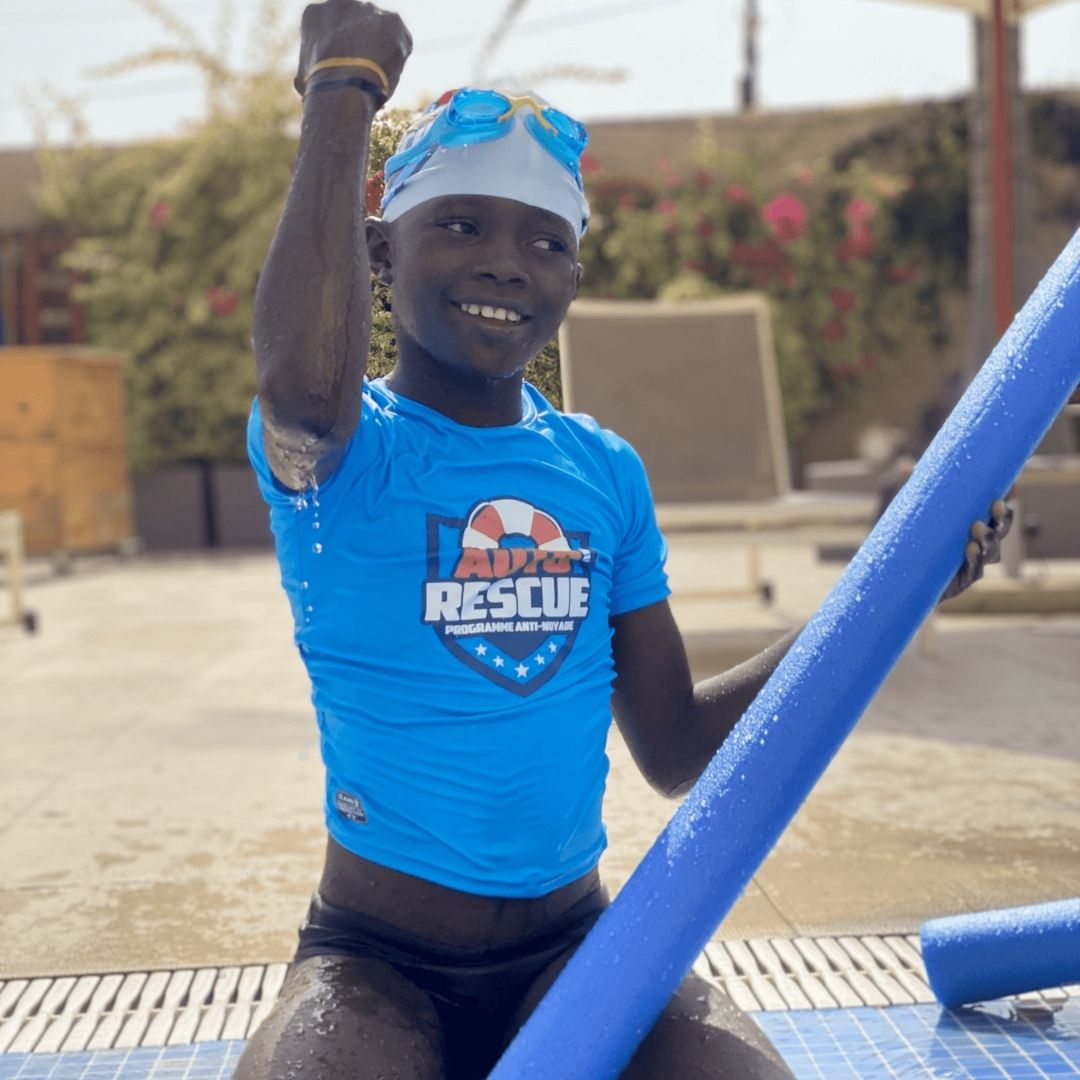 Enfant en t-shirt Auto-Rescue® levant le poing au bord de la piscine, Dakar 2021